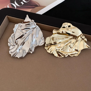 Detailed view of large gold and silver leaf brooches with crinkled metal texture in a box