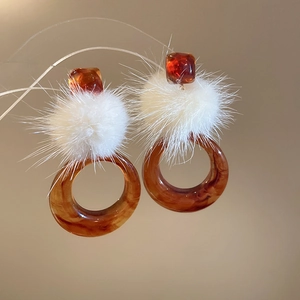 Dettaglio di orecchini a cerchio in resina con perle ambra e morbidi pompon bianchi