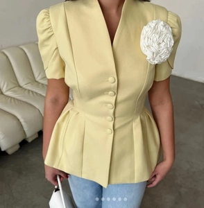 Détail d'un haut jaune clair à manches bouffantes avec fleur 3D blanche sur l'épaule