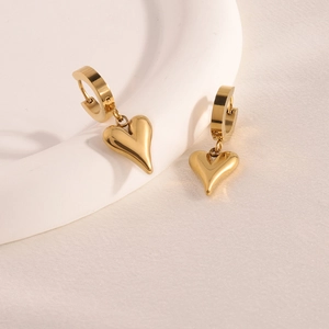 Close-up of gold heart drop earrings on a white ceramic plate with soft warm lighting