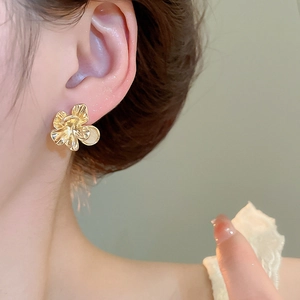 Close-up of golden flower stud earring with opal center worn on earlobe for detail