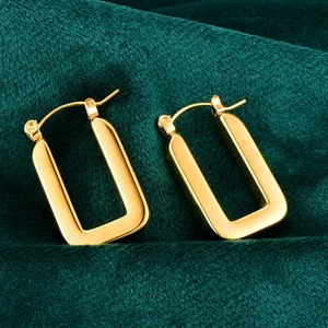 Close-up of gold-plated rectangular geometric hoop earrings on green fabric background