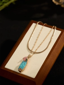 Detail of a vintage geometric necklace with blue crystal pendant and a pink charm detail