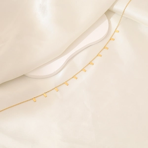 Macro shot of gold stainless steel geometric bar necklace on beige silk background