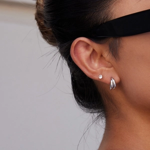 Close-up of geometric stainless steel stud earring and silver hoop on model's ear