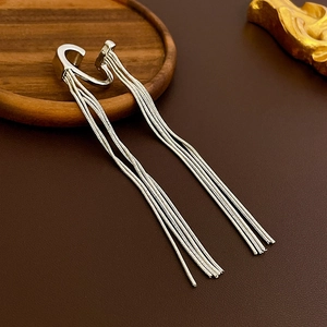 Detailed close-up of a silver long tassel ear cuff on a wooden coaster with leather background