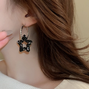Close-up of a black textured star hoop earring with sparkling sequins on a model