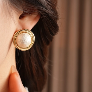 Close-up of a gold-plated twisted circular earring with a white textured cotton pearl