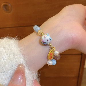 Detail of beaded bracelet with pearl, ceramic lucky cat charm, and gold engraved tag