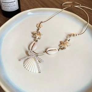 Böhmische Halskette mit Muscheln und Seesternen auf einem minimalistischen Keramikteller