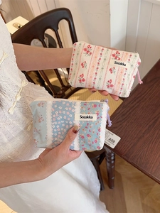 Floral fabric cosmetic bags in beige and blue patterns shown in hand for size