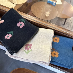 Close-up of folded knit scarves in black, beige, and blue with pink flower patterns