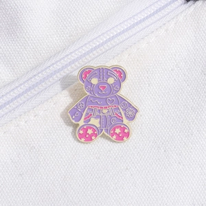 Detailed close-up of a purple bear enamel pin with colorful motifs on a white canvas bag