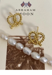 Macro detail of gold-plated twisted heart stud earrings and baroque pearl necklace