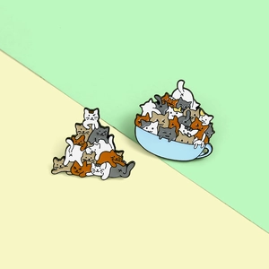Cartoon enamel pins featuring stacked cats and cats in a blue teacup on a split background