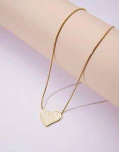 Detail of a gold heart pendant necklace with marble texture on a purple background