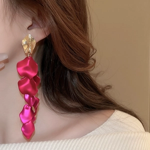 Close-up of long tassel earrings with golden leaves and vibrant rose red petals on a model