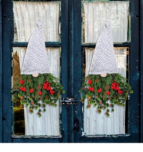 Two Christmas gnome ornaments with red berries and green plants on a blue glass door