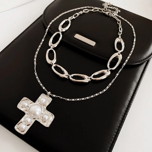 Detailed view of silver cross pendant with pearls layered on a black leather clutch bag