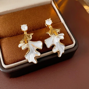 Macro shot of gold and white enamel leaf earrings with zircon in a brown jewelry box