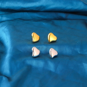 Polished 18K gold and silver heart stud earrings set on blue silk fabric background