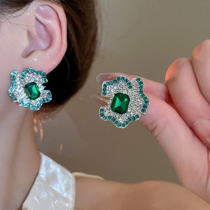 Macro detail of luxury flower earrings with emerald cut green stones and zircon accents
