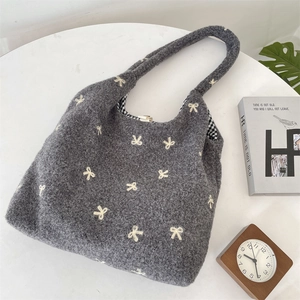 Close-up of grey plush tote bag with white bow embroidery and plaid lining on white table