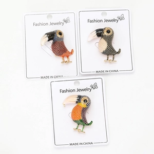 Three colorful enamel toucan bird brooches with rhinestones on white display cards