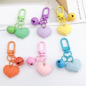 Macro shot of colorful matte heart bell keychains in pastel tones on a white wooden background