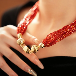 Dettaglio della collana multistrato con perline rosse tubolari e fibbia dorata