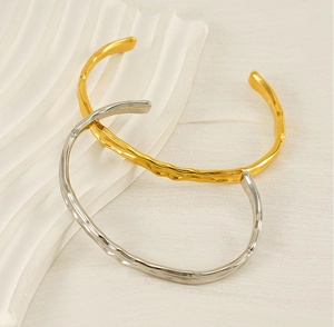 Close-up of gold and silver irregular lava texture cuffs on a wavy ceramic tray