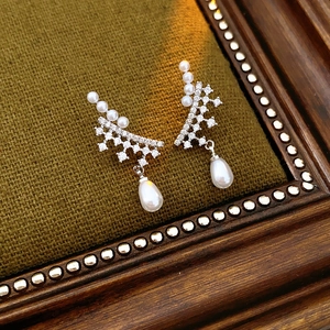 Detailed shot of silver drop earrings with pearls and zircons on a green velvet base