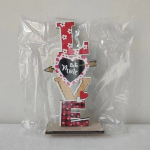 Close-up of wooden LOVE sign with red plaid and Be Mine heart on a rustic timber base