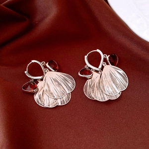 Close-up of rose gold petal earrings with deep red faceted gems on brown silk