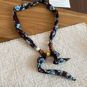 Detail of floral silk scarf necklace with colorful resin beads on a wooden table