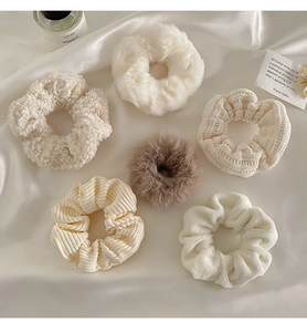 Close-up of assorted plush scrunchies in cream and beige on soft white satin fabric