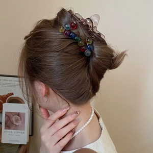 Detail of a brown resin hair claw clip decorated with colorful translucent beads on an elegant updo