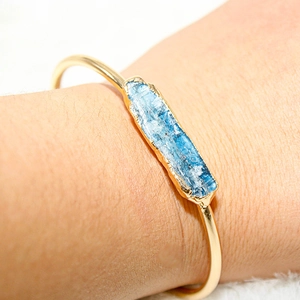 Close-up of gold plated adjustable cuff bracelet featuring raw blue crystal gemstone