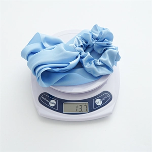 Blue satin scrunchie with streamer detail showing a lightweight 13.7g mass on a scale