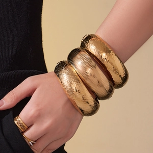 Textured gold-plated cuff bracelets with hammered and ribbed patterns on female model