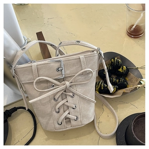 Gros plan du sac seau en toile beige avec détails à lacets et boucle en métal sur table