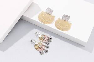 Détail de boucles d'oreilles fleurs ajourées et clous d'animaux sur décor minimaliste
