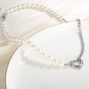 Detail of silver Cuban chain with white pearls and a hollow heart pendant on white silk