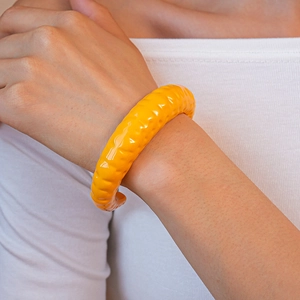 Dettaglio di un bracciale aperto giallo brillante con una moderna trama a onde irregolari