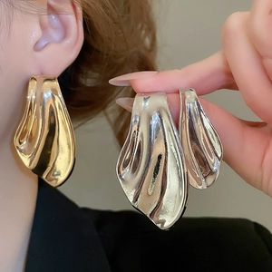 Macro detail of asymmetric metallic fishtail earrings with high-polish mirror finish