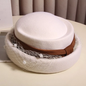Detail of white wool felt beret featuring a brown satin ribbon and mesh veil with pom-poms