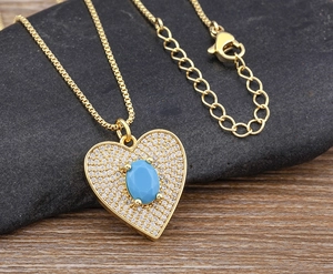 Detail of a gold heart pendant with a blue oval stone and box chain on pebbles