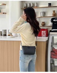 Detail of dark grey checkered crossbody bag with gold hardware on a casual model