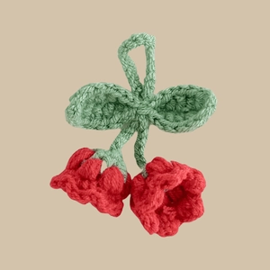 Macro shot of handmade crochet cherry charm featuring red bells and green leaves
