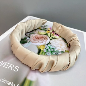 Detailed view of beige pleated satin headband placed on a magazine for a retro french look